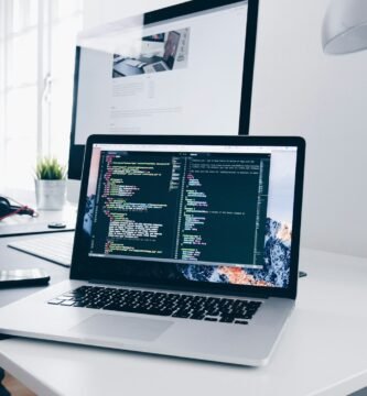 A MacBook with lines of code on its screen on a busy desk